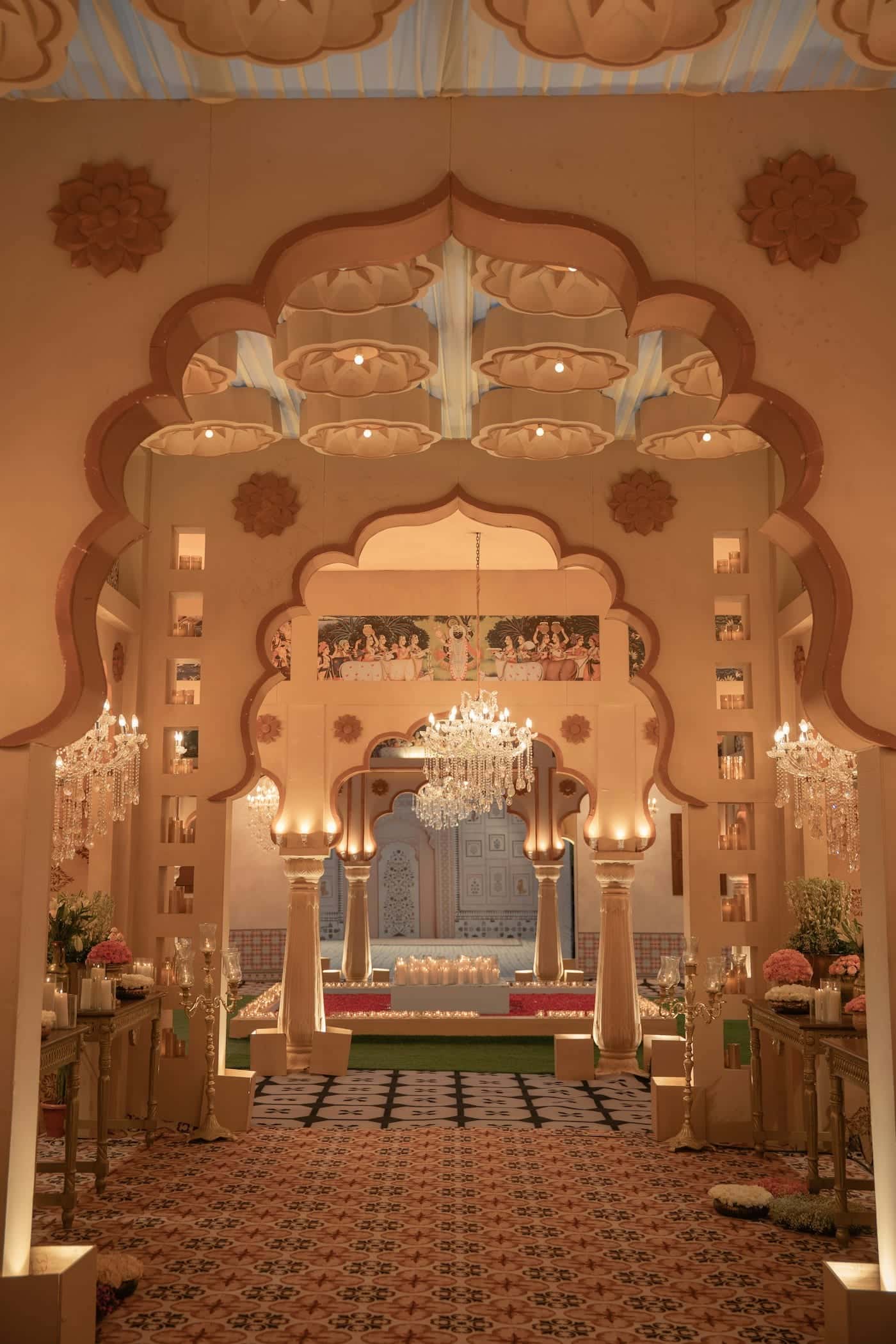Carved Rajasthani archway lit by chandeliers, opening onto a decorated wedding hall