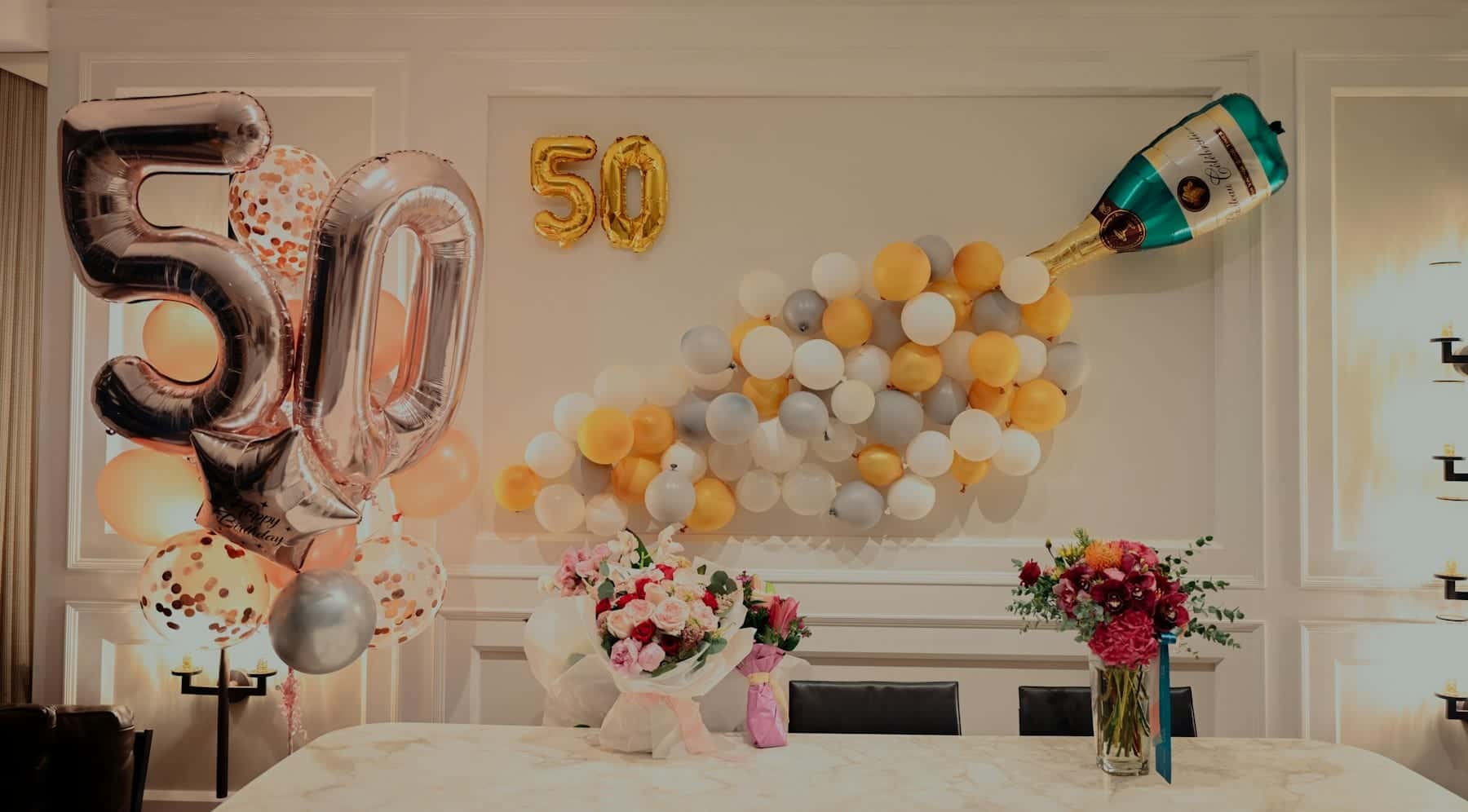 Number 50 balloons and a balloon champagne-bottle installation above a flower-lined dinner table