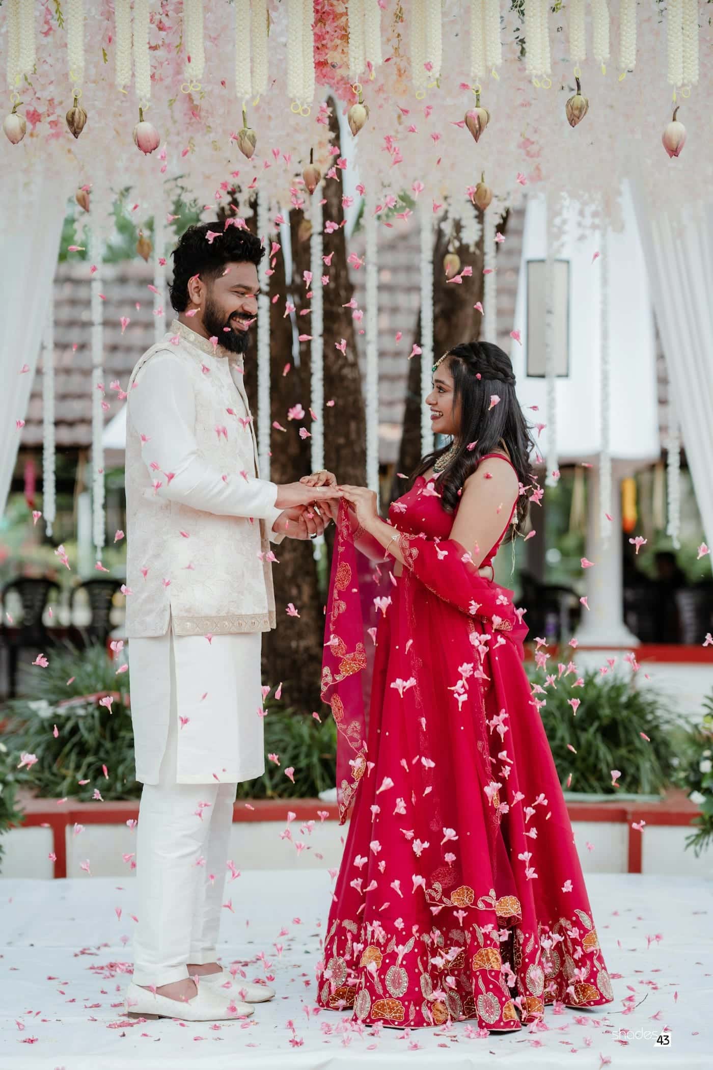 Couple exchanging rings beneath a canopy of hanging white and pink flowers
