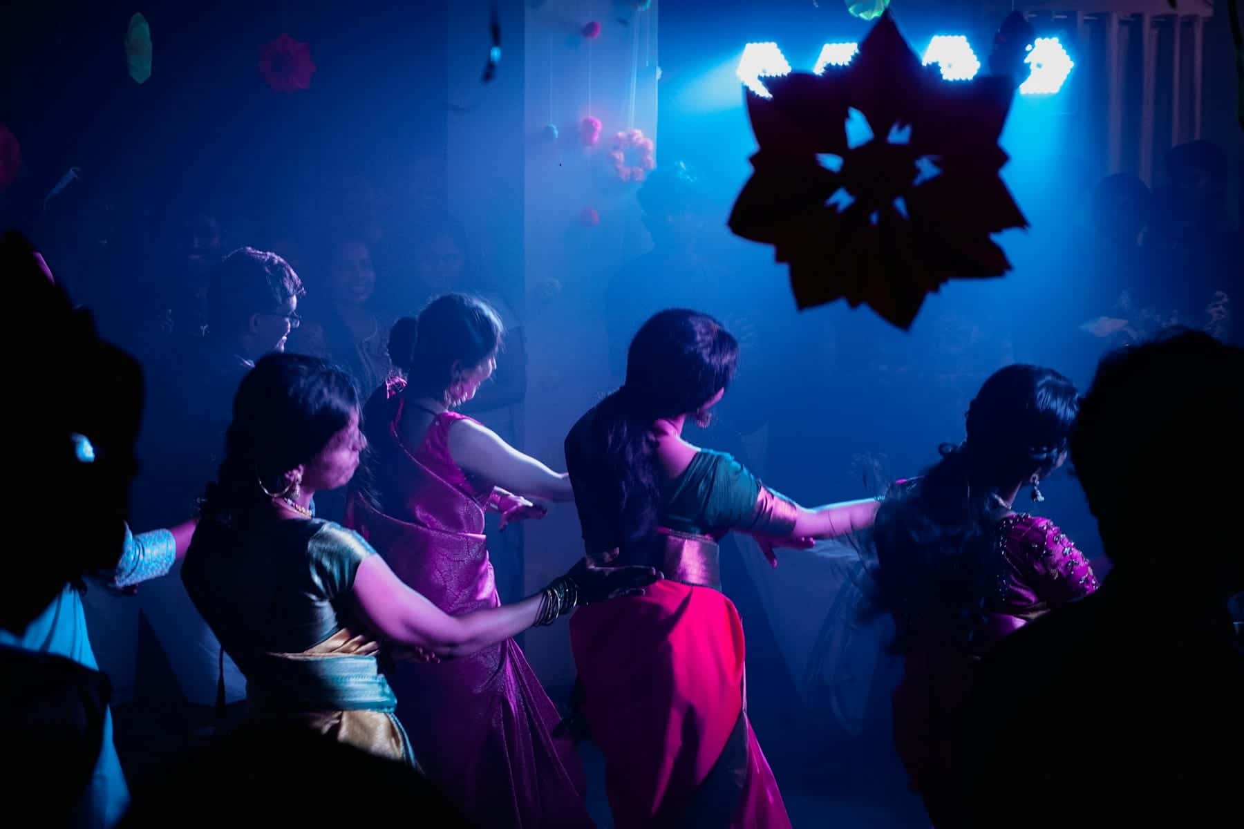 Women in saris dancing a choreographed routine under blue stage lights