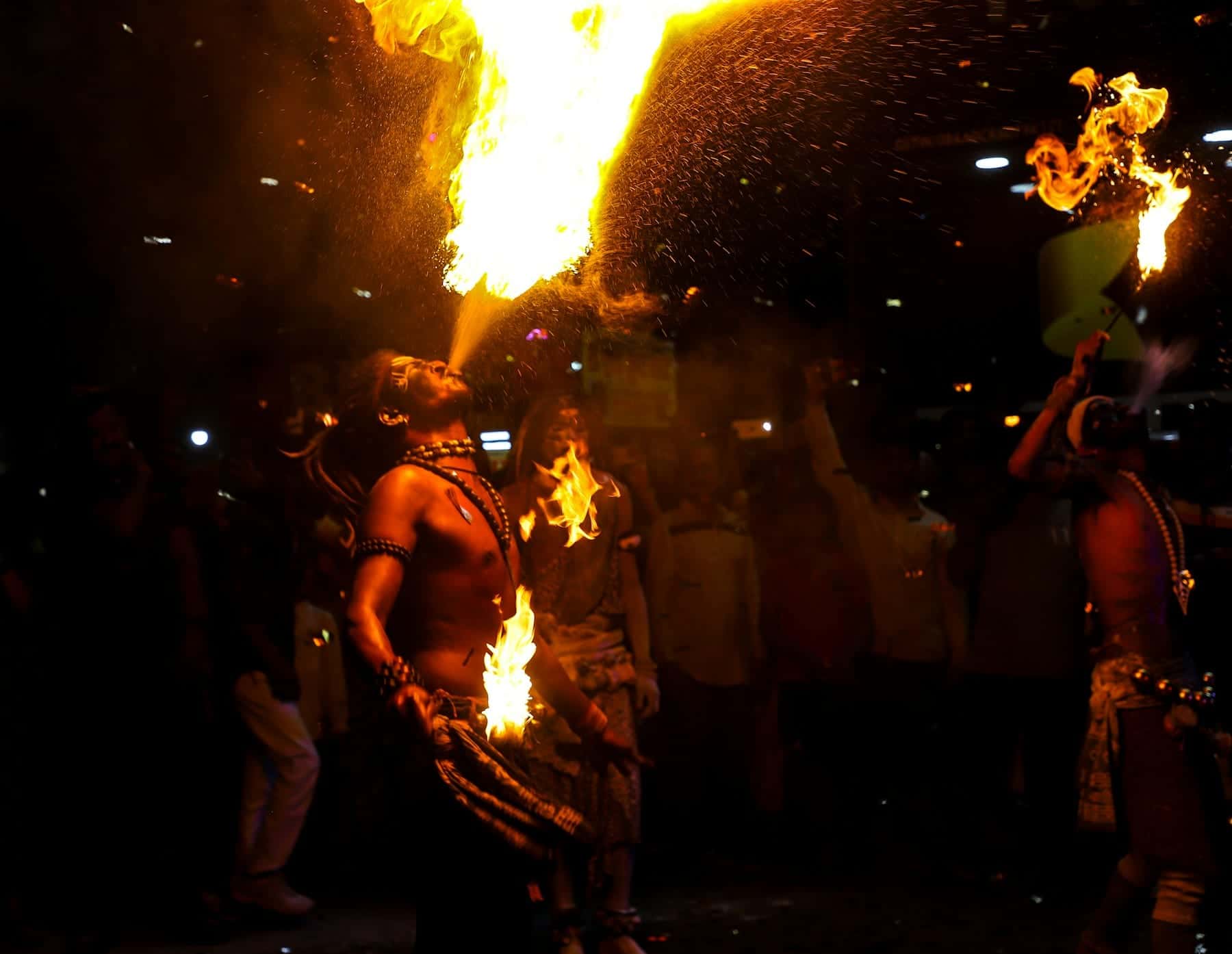 Fire performers breathing flames at night as guests gather to watch