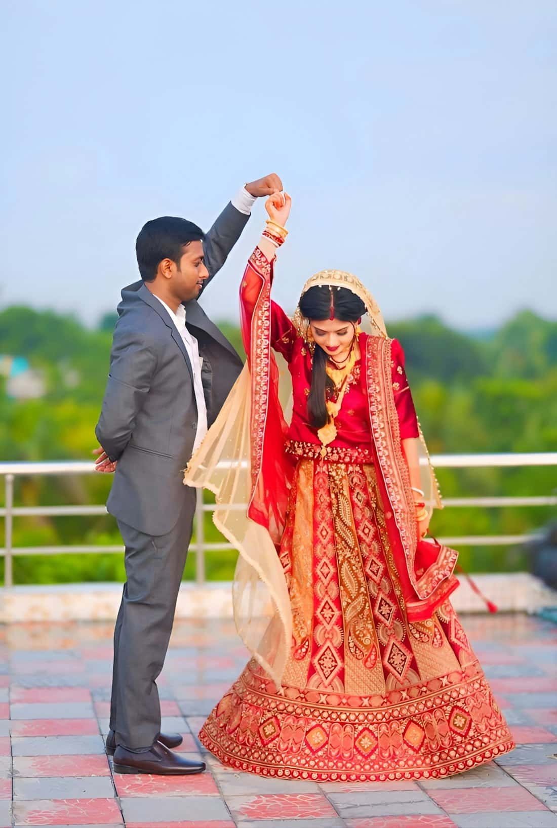Groom twirling his bride in a red and gold lehenga on an open terrace